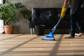 Jeune homme asiatique nettoyant le sol d'un salon à domicile